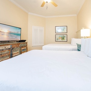 Relaxing guest bedroom featuring two comfortable queen beds, a large TV, and charming coastal decor