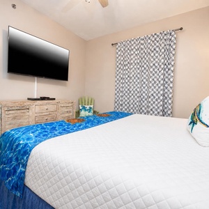 This bedroom features a large TV, a charming wooden dresser, and vibrant blue bedding, creating a relaxing retreat