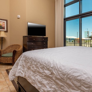 The master bedroom features a comfortable king bed, a TV for entertainment, and balcony access with beach views