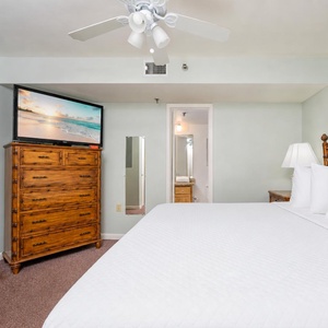 The bedroom features a large king bed with white linens, a wooden dresser, a TV, and an en-suite bathroom