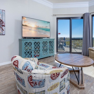 Cozy seating area features a colorful chair and recliner, with a TV and sliding doors leading to a balcony with gulf views