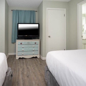 This guest bedroom features two queen beds, a vintage blue dresser, and a TV, with a bathroom visible in the background