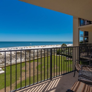 Enjoy the serene beachfront view from the balcony, featuring comfortable seating and a vibrant blue sky above