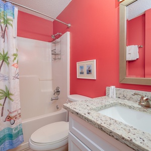 This extra full bath features vibrant red walls, a playful palm tree shower curtain, and a clean, bright vanity area