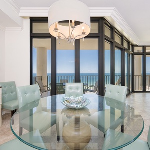 Bright dining area with mint green chairs and a stunning coastal view through floor-to-ceiling windows