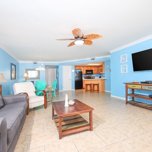 Living area features a gray sofa with queen sleeper, wooden coffee table, view of the beach and vibrant blue walls