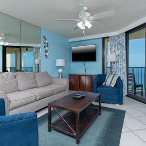 Living room features a gray sofa with a queen sleeper, blue accent chairs, and large windows showcasing the beach front view