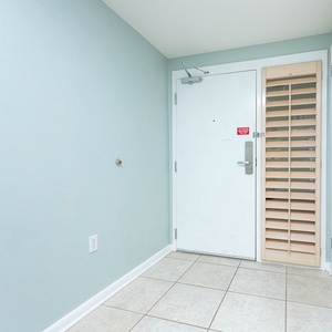 Welcoming entryway features soft blue walls, tiled flooring, and a stylish door with a wooden shutter for added privacy