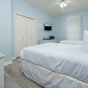 Rest comfortably in this serene guest bedroom featuring two cozy double beds, a TV, and soft natural light