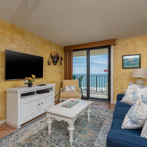 Living room featuring a cozy blue sofa with queen sleeper, a large TV, and a breathtaking view of the beach from the balcony