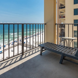 Relax on the balcony with a view of the serene beach and vibrant umbrellas under the clear blue sky
