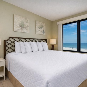 This bedroom features a large bed with plush pillows and a stunning beachfront view through the expansive window