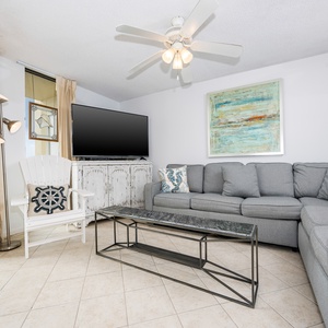Living area features a gray sectional sofa with queen sleeper, a decorative coffee table, and a view of the beach