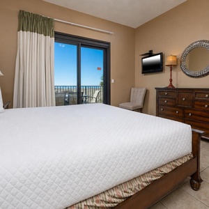 Inviting master bedroom featuring a king bed, dresser, and balcony access with views of the beach and clear blue skies