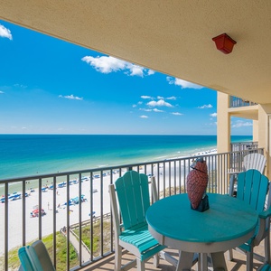 The balcony features turquoise seating and a table, offering a picturesque view of the beach and vibrant blue waters