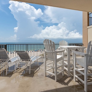 This spacious extended balcony features white outdoor furniture, perfect for enjoying the breathtaking beach view