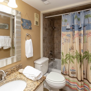 The bathroom features a stylish granite countertop, a beach-themed shower curtain, and fresh towels for a refreshing stay