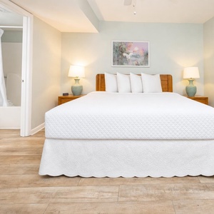 Bedroom featuring a king bed with plush pillows, bedside lamps, and a bathroom entrance visible in the background