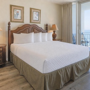 The master bedroom features a king bed with plush pillows and a stunning beachfront view through large sliding glass doors