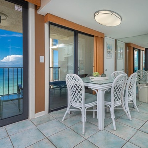 Bright dining area with a beach view, featuring a glass table and white wicker chairs, perfect for meals and relaxation