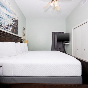 The serene bedroom features a king bed with crisp white linens, a mounted TV, and calming sea-inspired artwork on the wall