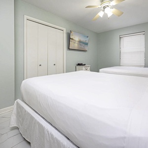 Bright guest bedroom featuring two queen beds, a wall-mounted TV, and light green walls, creating a refreshing retreat