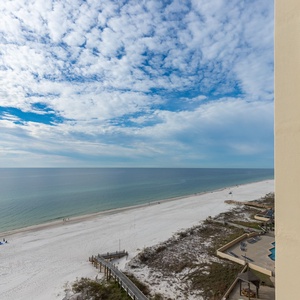 The view showcases a serene beachfront with white sand, gentle waves, and a clear blue sky, perfect for relaxation