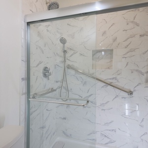 The walk-in shower features elegant marbled tile, a handheld showerhead, and shower rails for added safety and convenience