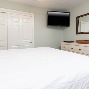 This guest bedroom features a cozy white queen bed, a wall-mounted TV, and stylish cabinetry for a relaxing retreat