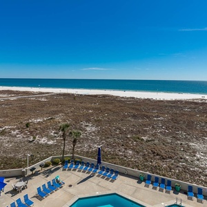 Expansive view of the beach with white sand, featuring a pool area and lounge chairs, framed by clear blue skies