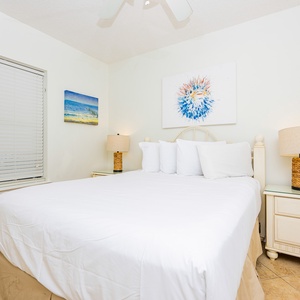 Rest in this comfortable guest bedroom featuring a large queen bed, beach artwork, and natural light from the window