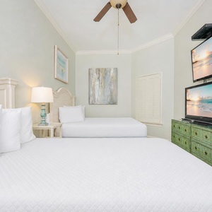 Guest bedroom featuring two queen beds, a stylish green dresser, and dual flat-screen TVs for entertainment