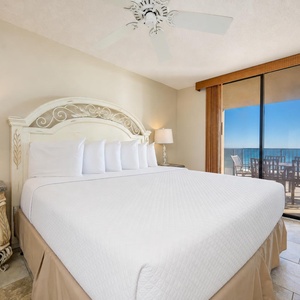 Bright master bedroom featuring a king bed, elegant furnishings, and a sliding door leading to the balcony with beach views