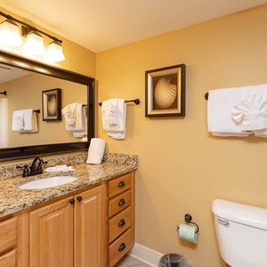 Warm yellow walls complement the granite countertop and elegant mirror in this guest bathroom with plush towels