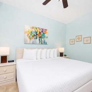 Brightly colored floral art complements the light blue walls in this serene bedroom featuring a plush king bed