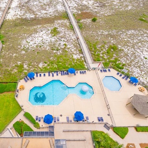 Aerial balcony view showcasing the pool area with lounge chairs, leading to a pathway that connects to the beach