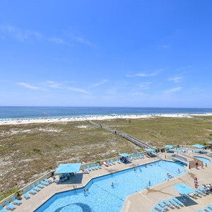 Stunning view of the beach and turquoise waters from the balcony, overlooking the inviting pool area and lounge chairs