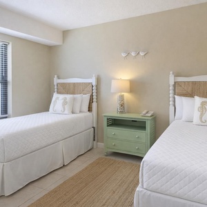 Charming guest room with two twin beds, a light green nightstand, and coastal decor
