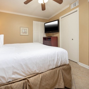 Cozy bedroom featuring a plush king bed, a wall-mounted TV, and warm beige walls creating a relaxing atmosphere