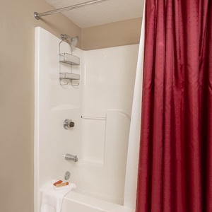 Tub/shower combo with a red curtain in the guest bath, white towels, and a sleek design, offering a refreshing space