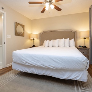 A serene guest bedroom features a plush king bed with decorative pillows, soft lighting, and elegant gray curtains