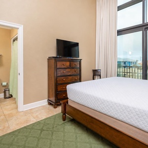 This bedroom features a cozy king bed, a TV for entertainment, and large windows offering a bright view