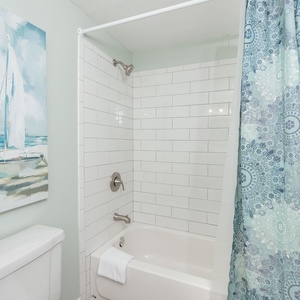 Guest bathroom features a tub/shower combo with a colorful patterned curtain and a serene coastal painting on the wall