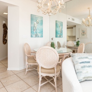 Bright dining area features a round glass table surrounded by rattan chairs, with coastal artwork enhancing the relaxed vibe