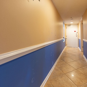 Welcoming hallway features a mix of warm beige and vibrant blue walls, leading to the entrance door with a tile floor