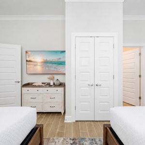 Inviting guest bedroom featuring two queen beds, a stylish dresser, and a large TV