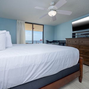 Comfortable master bedroom featuring a king bed, baby crib, mounted TV, and a balcony with a beach view