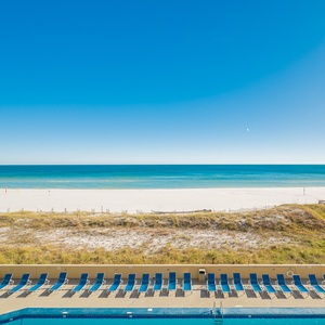 Enjoy a serene view of the beach and turquoise waters from the balcony, with lounge chairs lining the pool area below