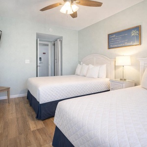 This guest bedroom features two comfortable beds, a mounted TV, and a soothing color palette for a relaxing stay