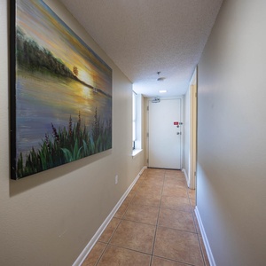 Bright hallway featuring a serene landscape painting, leading to the entrance door and a window allowing natural light